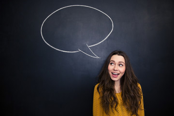 Cheerful woman smiling over blackboard with empty speech bubble