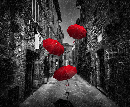Fototapeta Umrbellas flying with wind and rain on dark street in an old Italian town in Tuscany, Italy