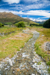 New Zealand's landscape with small stream or brook in foreground and snow capped mountains in background on a sunny summer day