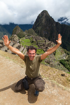 Viaggiare: ragazzo caucasico sorride a braccia alzate nelle rovine del sito archeologico di Machu Picchu, Peru