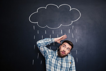 Unhappy man hiding from rain drawn on blackboard background