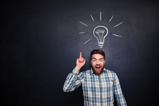 Excited man pointing up over blackboard background with light bulb