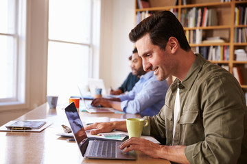 Businessman Using Laptop At Desk In Busy Office