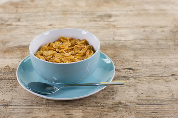 Frühstück aus Kornflakes. Eine Portion Kornflakes in blauer Schale auf blauem Teller mit Löffel. Auf hellem Holztisch