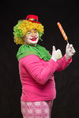 Cheerful funny clown in a hat with a big candy