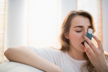 Woman using her inhaler on couch - obrazy, fototapety, plakaty