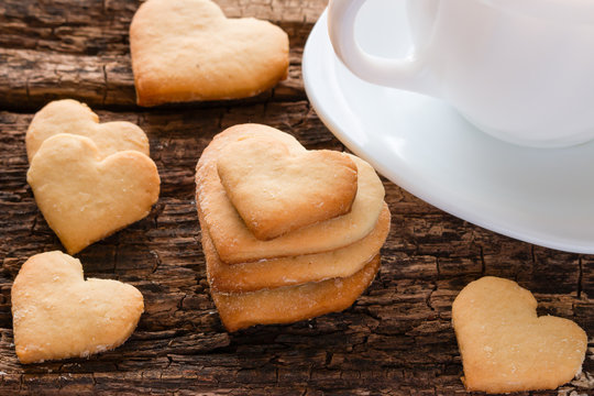 homemade cookies in the shape of heart and white cup on a wooden background