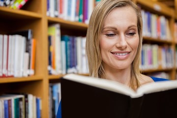 Happy female student reading a book in the library