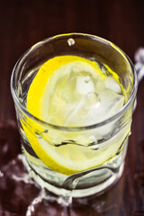 Water splash in glasses with lemon slice and ice cube, on wooden table