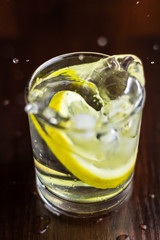 Water splash in glasses with lemon slice and ice cube, on wooden table