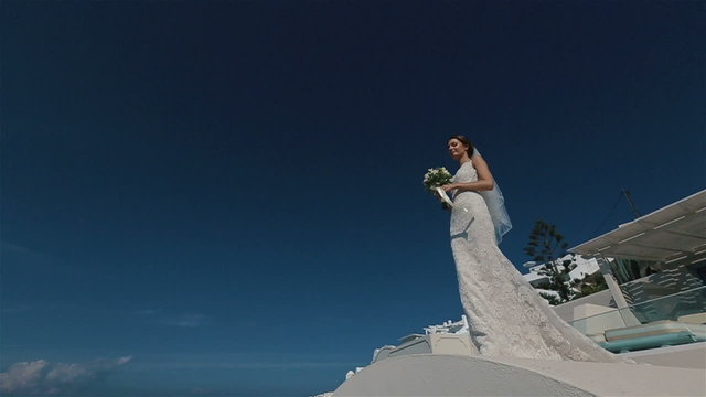 Beautiful sexy brunette bride in wedding dress with bouquet in her hands moves on the roof, Santorini closeup