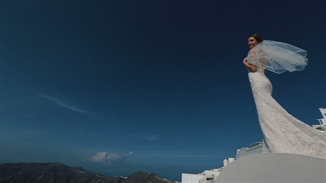 Beautiful sexy brunette bride in wedding dress with bouquet in her hands moves on the roof, Santorini closeup