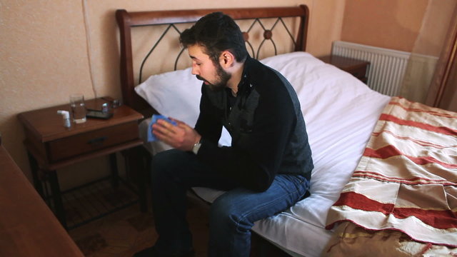 Sick man taking  pill while sitting on bed. Dynamic shot