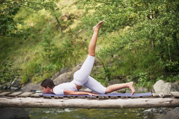 Beautiful young woman meditating in yoga pose at a mountain stream. Selective focus on woman.