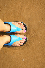 Fototapeta na wymiar female foot in flip flops on the beach