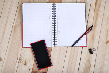 Red Smart Phone With Blank Black Screen, Notepad And Pencil On Wooden Desk.
