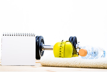 Sport Equipment. Dumbbells,  Towel, Apple, Tape Measure, Orange Juice And Notepad To Workout Plan On Wooden Table With White Background. 