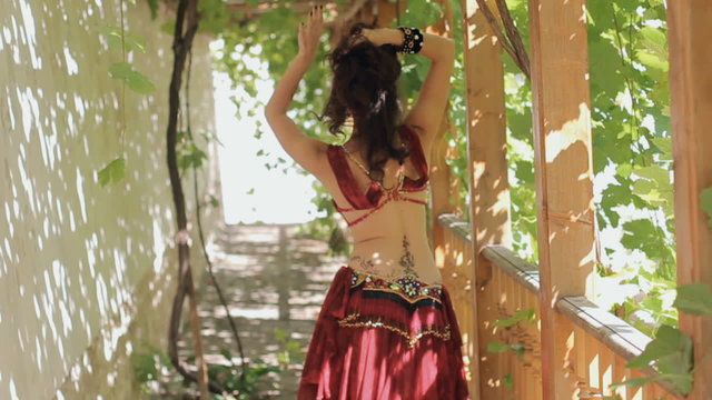 Attractive woman with tattoos dancing belly dance in gazebo overgrown with vines