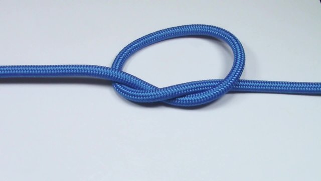 Simple overhand knot made from blue synthetic rope, tightening on white background