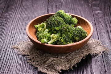 Bunch of fresh green broccoli on brown plate over wooden background