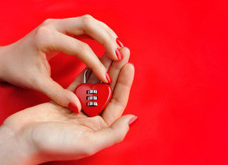 Padlock heart-shape in women's hands on red background
