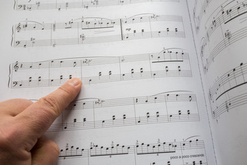 Naklejka premium Finger pointing to sheet music. Good file for musical backgrounds. shallow DOF