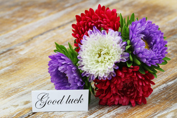 Good luck card with colorful aster flowers bouquet on rustic wooden surface
