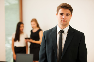 Young Business man standing in first plain with coworkers in background
