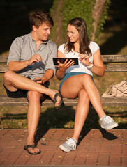 Young couple having fun on a bench in park while socializing ove