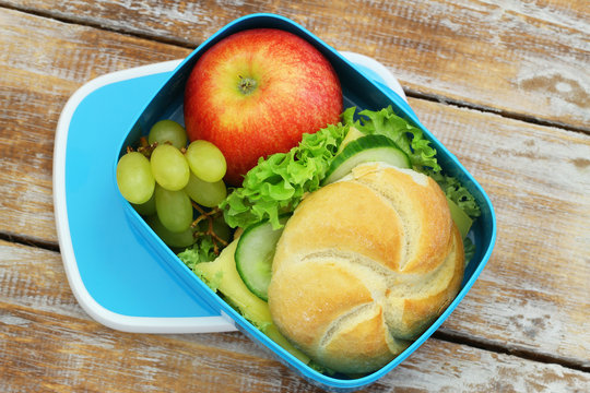 Lunch box containing bread roll with cheese and lettuce, grapes and red apple
