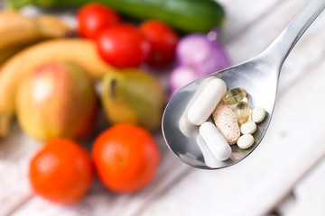Silver spoon with dietary supplements on fruity background