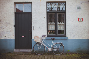 Fototapeta na wymiar White bicycle standing near the brick facade of the house
