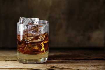 glass of scotch whiskey with ice cubes on a rustic wooden table