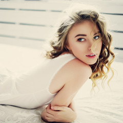 Portrait of a beautiful young girl with blonde curly hair in lingerie lying on the bed