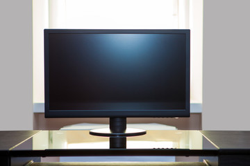 a computer monitor is in a room, on a table opposite a window