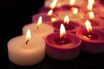 Many burning small candles on dark background, close-up