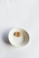 Single sugar cube left in a small bowl on white background