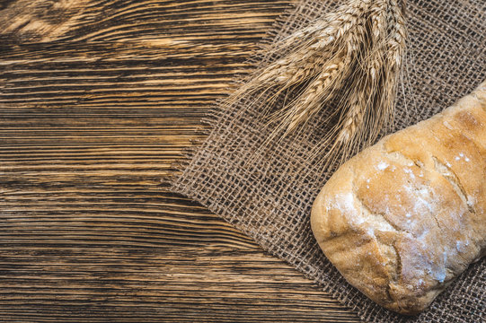 a ciabatta bread with wheat on stackcloth on a wooden rustic background
