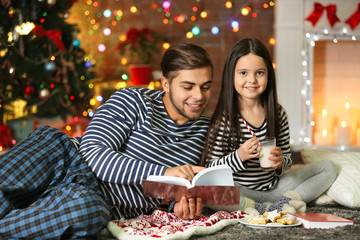 Older brother with little sister reading book and eating cookies in Christmas living room