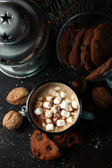 Mug of hot cacao with marshmallow, cookies and lantern on black table