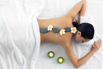 Obraz na płótnie Canvas Spa concept. Woman relaxing with pebbles and plumeria flowers on her back