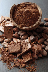 Bowl with aromatic cocoa beans and chocolate on grey background, close up