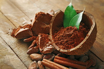Bowl with aromatic cocoa powder and green leaf on wooden background, close up