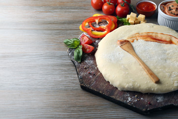 Fresh dough prepared for pizza with tomatoes and sliced pepper on a wooden board, close up