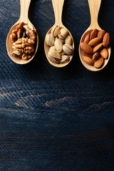 Spoons with walnuts, pistachios and almonds, on grey wooden background