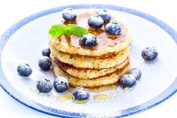 Pile of pancakes with blueberries sprinkled with icing sugar and poured on with honey