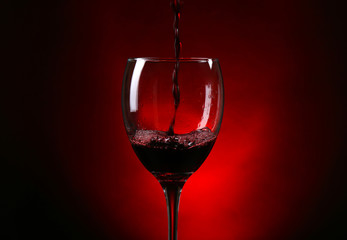 Wine pouring in glass on dark red background