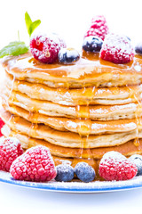 Pile of pancakes with blueberries and raspberries sprinkled with icing sugar and poured on with honey
