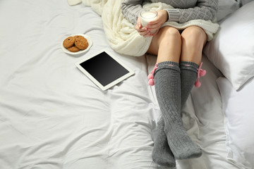 Woman with tablet drinking milk on her bed
