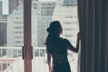 カーテンを開けて景色を見ている女性